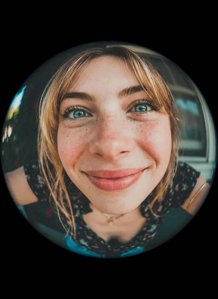 Comical selfie with an extreme fisheye lens, exaggerated nose and cheeks, circular bubble frame, flattering soft light, vibrant grading, slight vignetting, background outside fisheye is pure black, no text